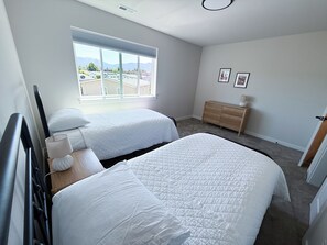 Un dormitorio con dos camas, un aparador y una ventana con vistas a edificios y montañas.
