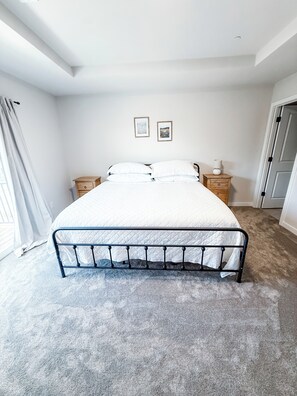Un dormitorio con cama, dos mesitas de noche, una puerta y una ventana con cortinas.