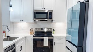 A modern kitchen with white cabinets, stainless steel appliances, and a patterned rug. - New Sequim Condo Near Olympic Discovery Trail, Golf & Lavender Farms (Sequim)
