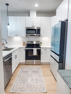 Una cocina moderna con gabinetes blancos, electrodomésticos de acero inoxidable, microondas, horno y refrigerador.