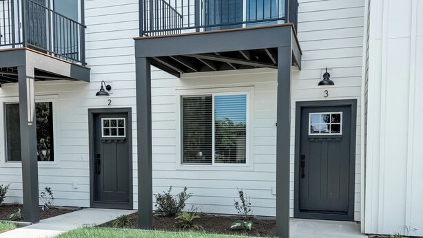 A two-story residential building with a balcony, a front door, and a small garden area. - New Sequim Condo Near Olympic Discovery Trail, Golf & Lavender Farms (Sequim)