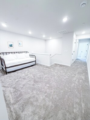 Ein Schlafzimmer mit Bett, weißen Wänden, Teppichboden und einer Tür zu einem weiteren Raum.