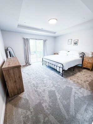 Un dormitorio con cama, cómoda de madera, mesita de noche, lámpara de techo, ventana con cortinas y puerta.