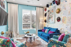 Ein Wohnzimmer mit einem blauen Sofa, floralen Sessel, einem Globus auf einem Beistelltisch und einem großen Fenster mit Vorhängen.
