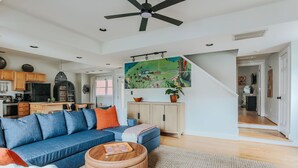 A modern living room with a blue sofa, wooden coffee table, and a large painting above the fireplace. - Oasis on 5th (Charlottesville)