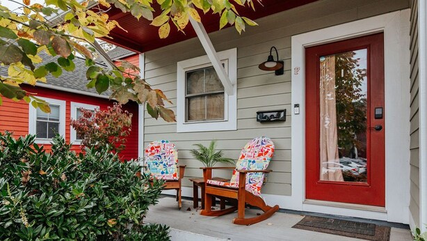 A house with a red door, a porch with two rocking chairs and a small table, and a window above the door. - Oasis on 5th (Charlottesville)