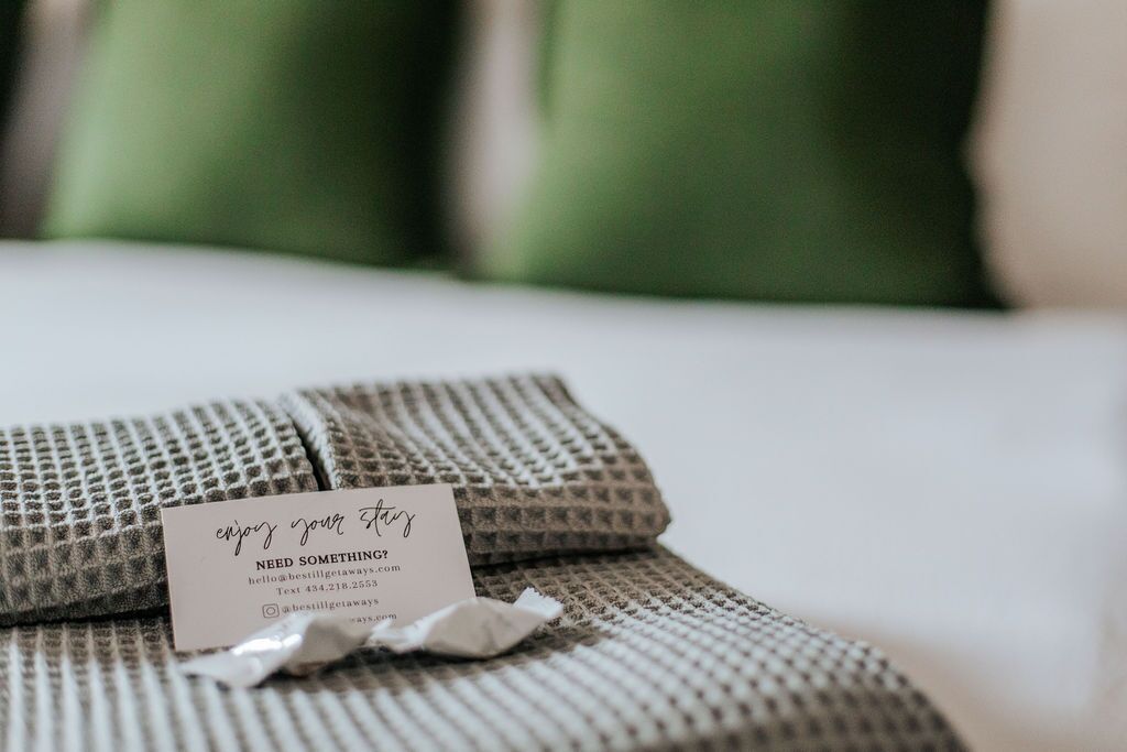 A neatly folded bedspread with a tag that reads "enjoy your stay" and "NEED SOMETHING?" along with contact information.