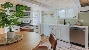 Una cocina moderna con armarios blancos, techo de madera y zona de comedor con una mesa y sillas.