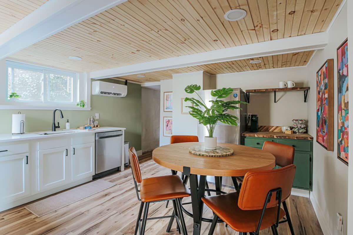 A modern kitchen with white cabinets, a wooden dining table, and a potted plant.