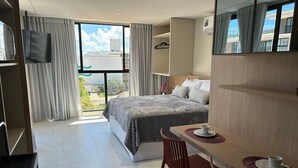 Ein Hotelzimmer mit Bett, Schreibtisch mit Tasse, Stuhl, Fernseher und großem Fenster mit Vorhängen.