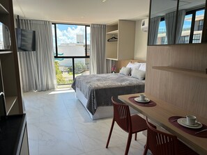 Ein Hotelzimmer mit Bett, Schreibtisch mit Tasse, Stuhl, Fernseher und großem Fenster mit Vorhängen.