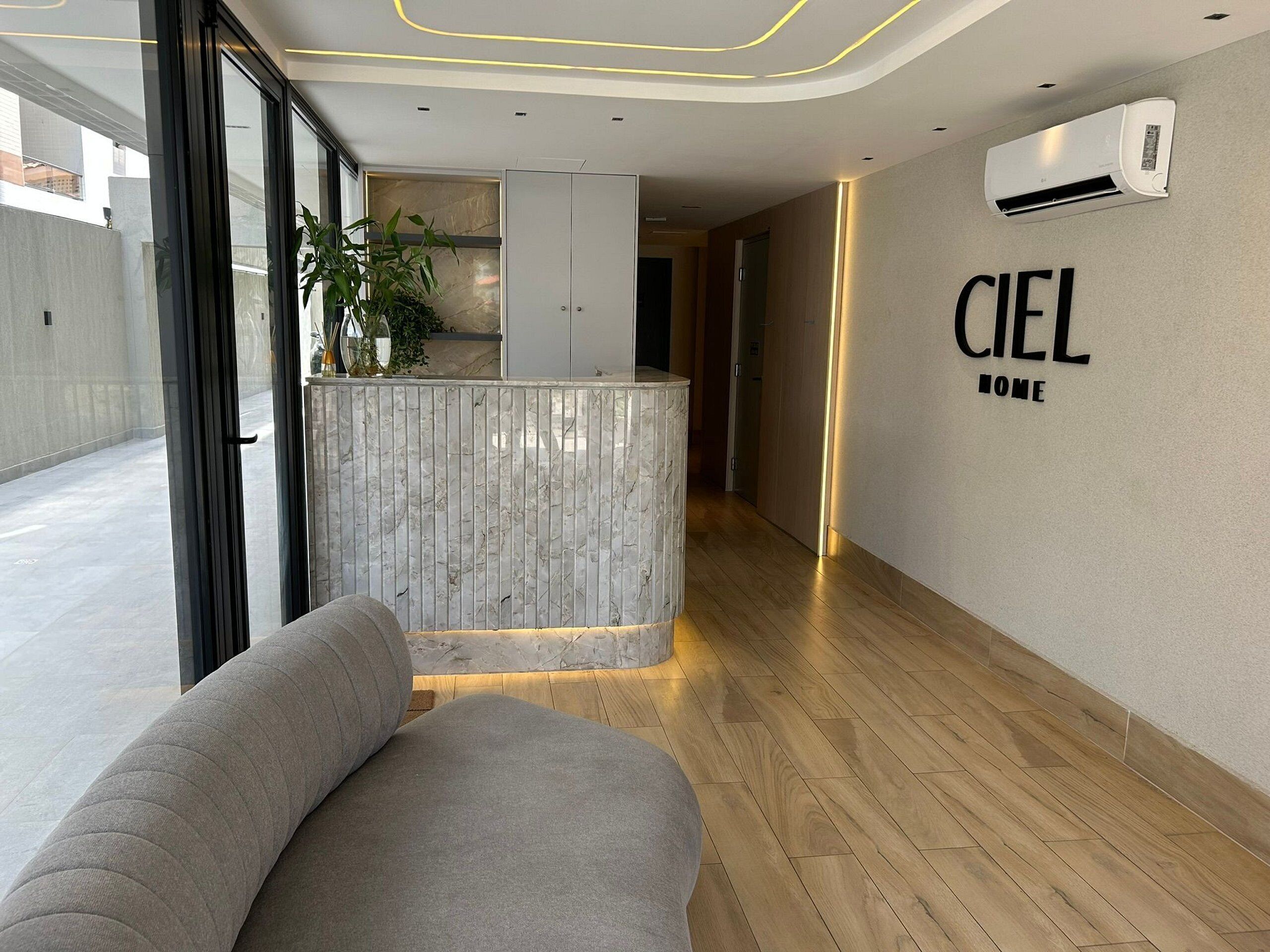Eine moderne Hotellobby mit einer Rezeption, einer Sitzecke, einem Blumentopf und einer Klimaanlage an der Wand.