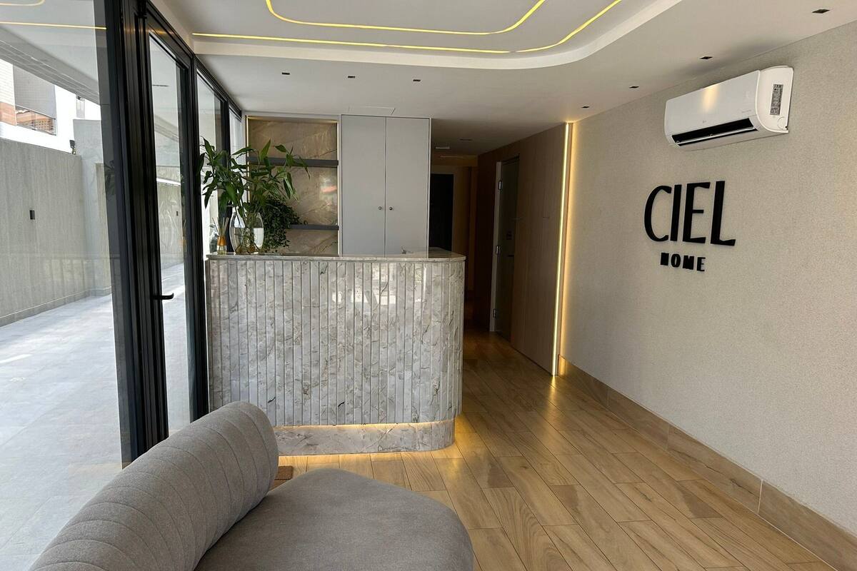 A modern hotel lobby with a reception desk, a sofa, a potted plant, and an air conditioning unit on the wall.