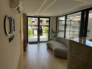 Eine moderne Hotelhalle mit einer Couch, einer Rezeption und einem großen Glasbalkon zur Außenwelt.