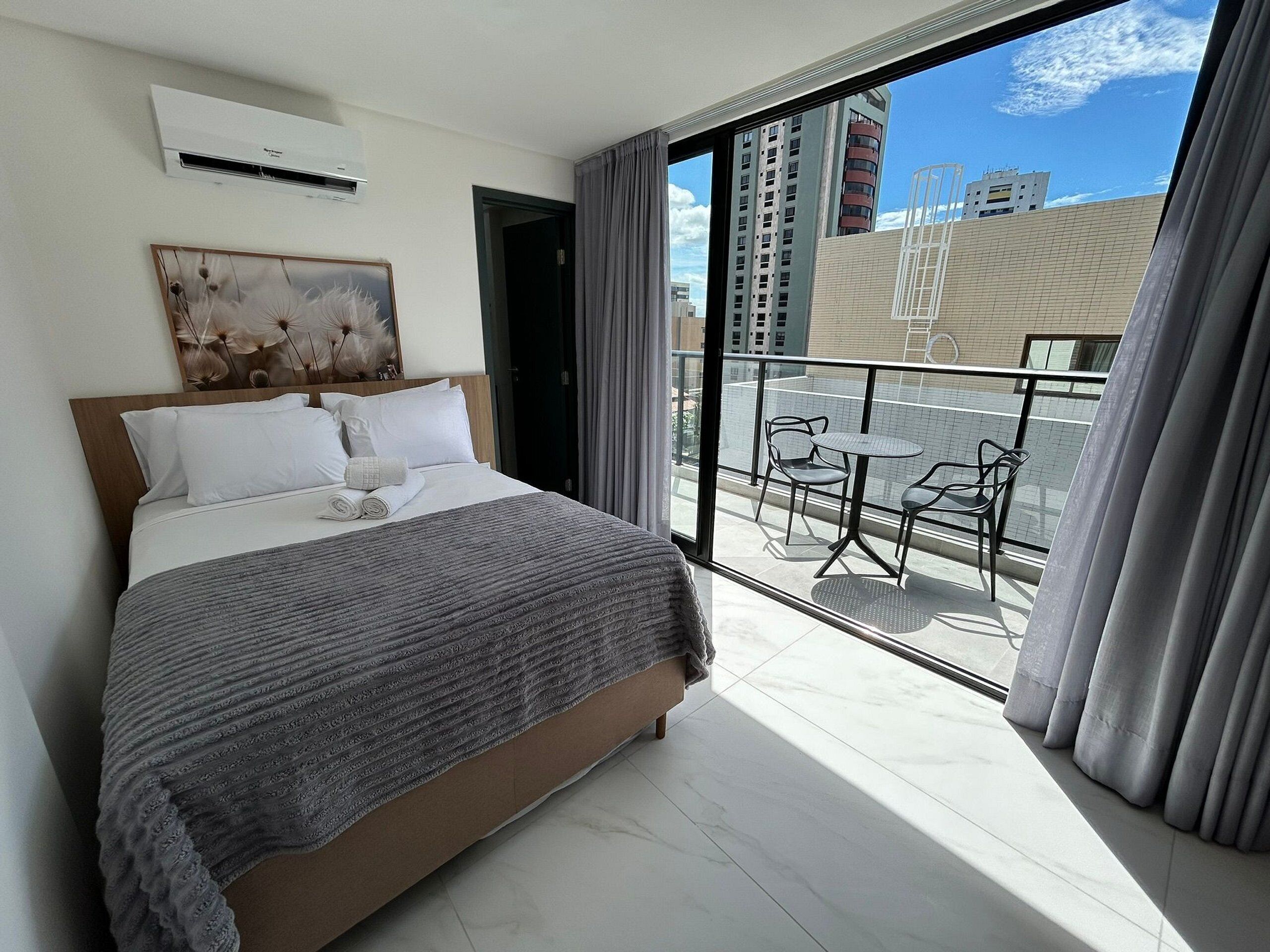 Ein Hotelzimmer mit einem großen Bett, einem Bild an der Wand und einem Balkon mit Tisch und Stühlen.