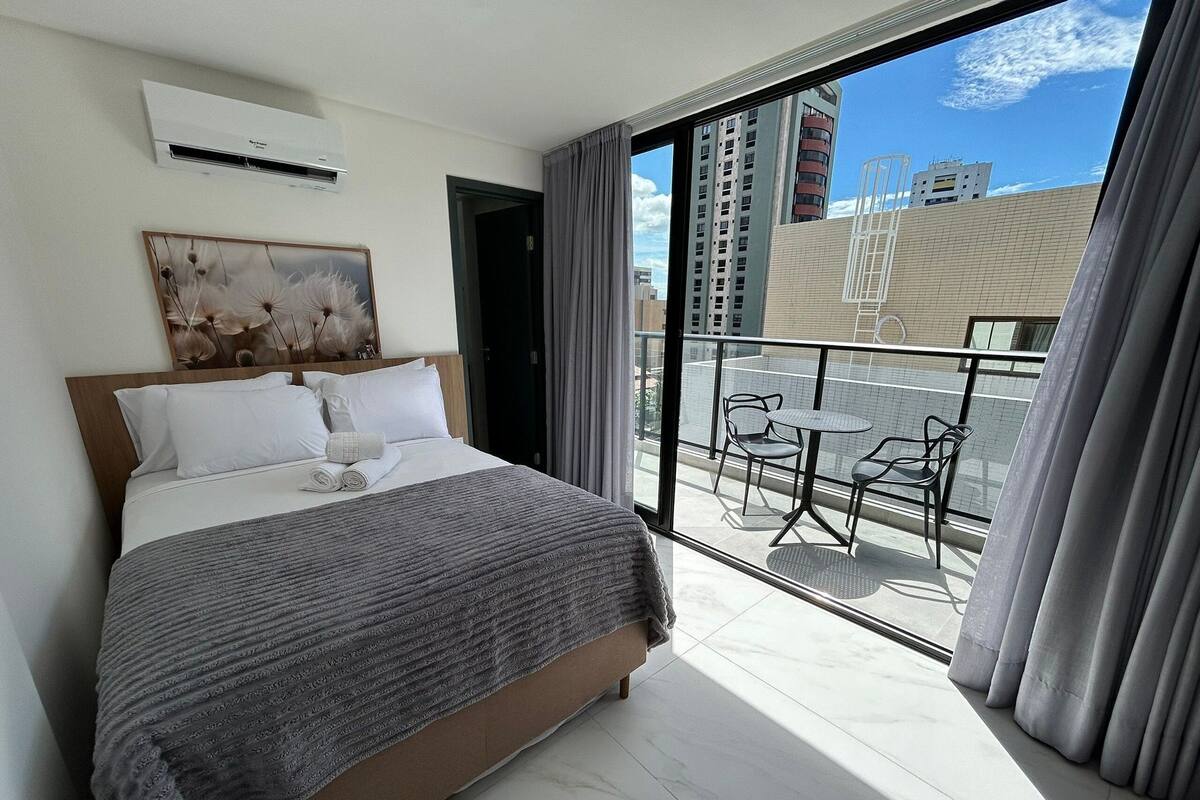 A hotel room with a large bed, a painting on the wall, and a balcony with a table and chairs.