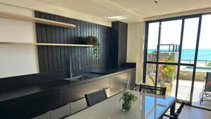 Eine moderne Küche mit schwarzem Arbeitsplatz, integriertem Spülbecken und einem Essbereich mit Glastisch und Stühlen.