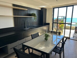 Eine moderne Küche mit schwarzem Arbeitsplatz, integriertem Spülbecken und einem Essbereich mit Glastisch und Stühlen.