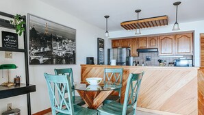 Una cocina moderna con armarios de madera, una mesa de comedor de vidrio y sillas color verde azulado.
