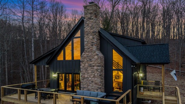 A modern cabin with a stone chimney, large windows, a deck with outdoor furniture, and a staircase leading to an upper level. - Pilotview Hollow (Nellysford)