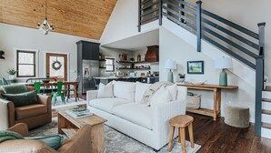 A spacious living area with a high ceiling, a staircase, and a kitchen in the background. - Pilotview Hollow (Nellysford)