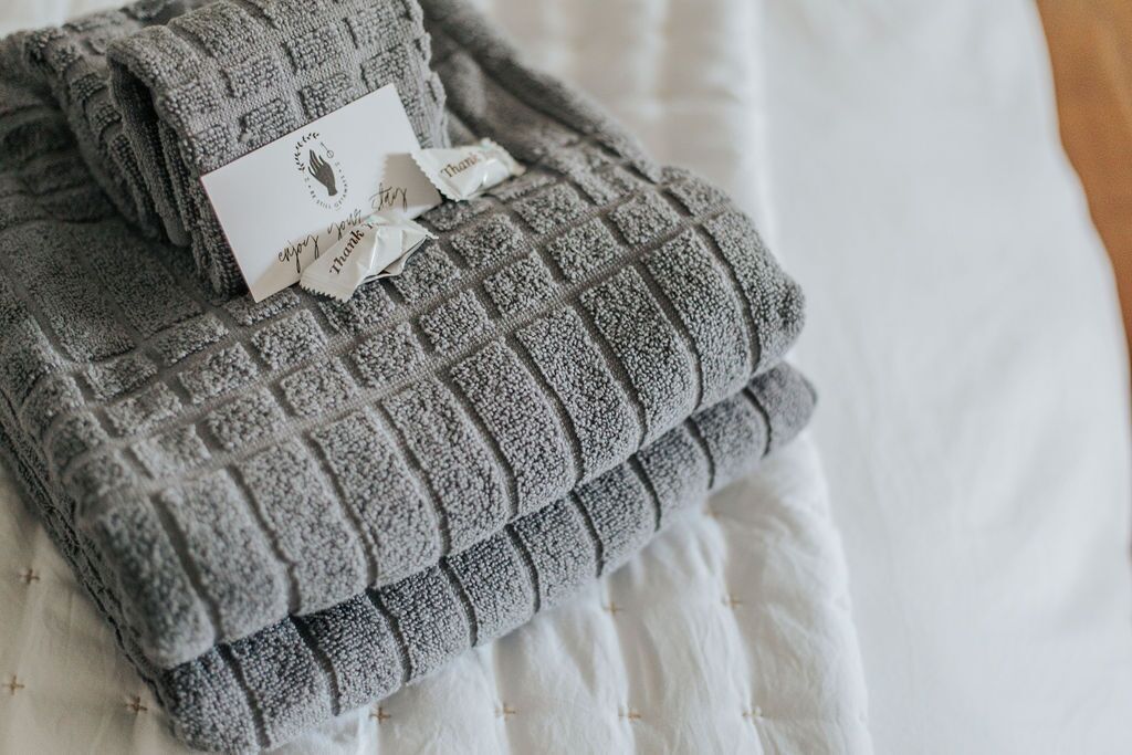 A neatly folded gray towel with a tag on a white bedspread.