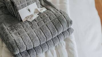 A neatly folded gray towel with a tag on a white bedspread.