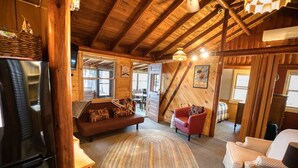 A cozy cabin interior with a wooden ceiling, a sofa, a red chair, and a dining table. - Charming 3-bedroom lakefront cabin with AC in Hayward Wisconsin! (Hayward)