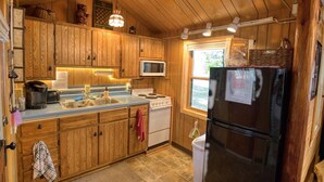 A kitchen with wooden cabinets, a stove, a microwave, and a refrigerator. - Charming 3-bedroom lakefront cabin with AC in Hayward Wisconsin! (Hayward)