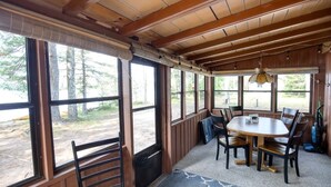 A wooden interior with a dining table and chairs, large windows, and a ceiling fan. - Charming 3-bedroom lakefront cabin with AC in Hayward Wisconsin! (Hayward)