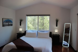 Camera da letto con un letto, due comodini con lampade, un'ampia finestra vista alberi e uno specchio.