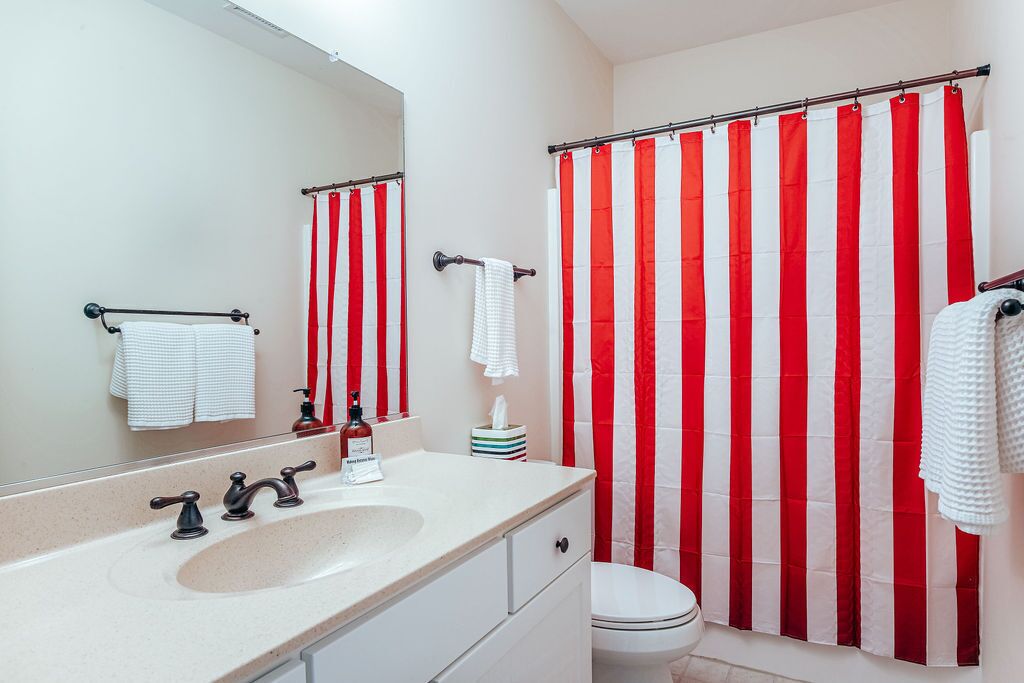 Un bagno con lavandino, specchio, portasciuga e tenda da doccia a righe.