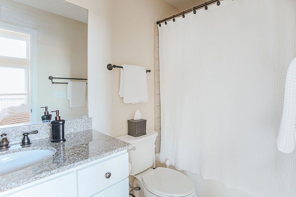 A bathroom with a granite countertop sink, a mirror, a toilet, and a shower curtain.