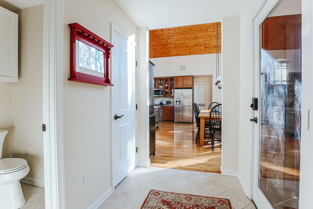A hallway leading to a kitchen with wooden flooring, a dining area, and a red-framed picture on the wall.
