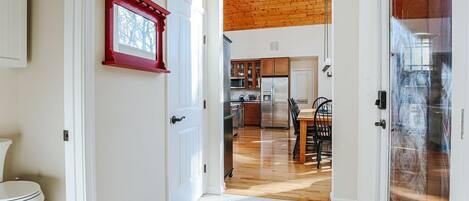 A hallway leading to a kitchen with wooden flooring, a dining area, and a red-framed picture on the wall.