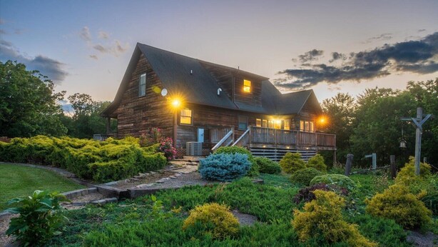A rustic wooden house with a porch, surrounded by well-maintained gardens and a cross in the yard. - Ridgeview Retreat (Staunton)