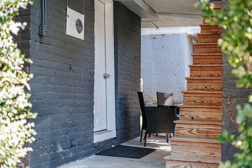 A staircase leading to a wooden door, a black wicker chair, and a small table under a covered area.