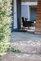 Un patio de hormigón con un banco de madera y una mesa, rodeado de vegetación.