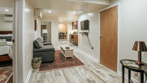 Un espace de vie compact comprenant un canapé, une petite table, un téléviseur fixé au mur et une porte en bois.