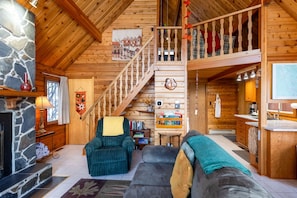 LâintĂ©rieur dâun chalet en bois comprend une cheminĂ©e, un escalier, un salon avec des canapĂ©s et un coin cuisine.