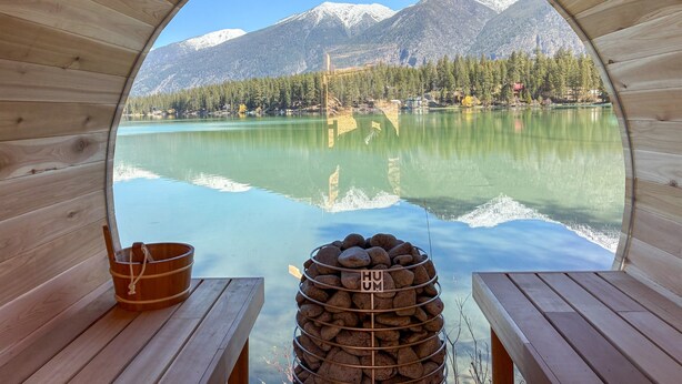 A wooden cabin with a circular window overlooking a lake and mountains.