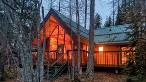 A cabin with a wooden exterior, a staircase leading to the entrance, and a metal roof.