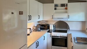 Une cuisine compacte avec des meubles blancs, un four encastré, un four à micro-ondes et une bouilloire.