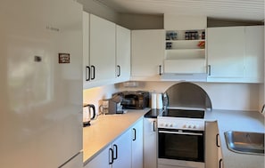 Una cocina compacta con armarios blancos, horno integrado, microondas y hervidor.