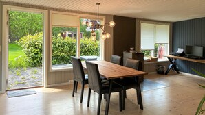 Un coin repas avec une table et des chaises en bois, un luminaire suspendu et une vue sur la verdure à l’extérieur.