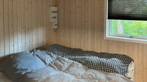 Un lit simple avec une couverture à carreaux noirs et blancs, un oreiller blanc et un mur en bois avec une fenêtre.