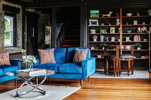 A cozy living room with a blue sofa, wooden bookshelves, and a staircase.