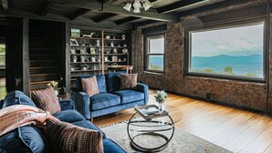 Una sala de estar con un sofá azul, una estantería y un ventanal con vistas.
