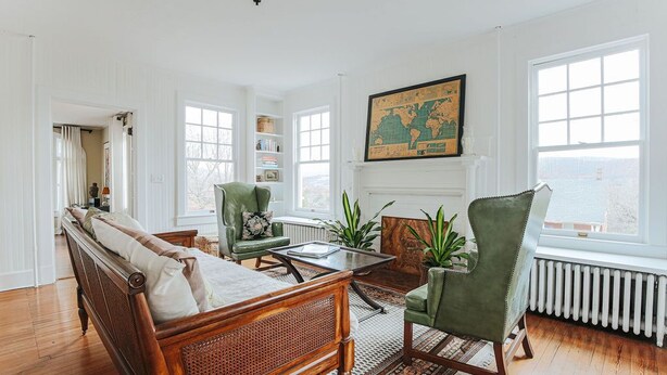 Un salón espacioso con un sofá de madera, sillones verdes, una mesa de centro y un gran mapa del mundo en la pared.