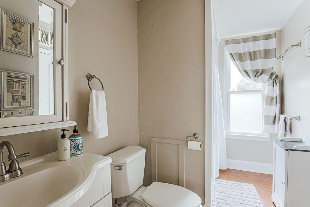 A bathroom with a white sink, toilet, and shower curtain. There are framed pictures on the wall and a window with a view.